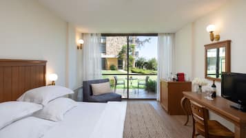 A hotel room with a bed, a desk, a television, and a view of the garden through the glass door.