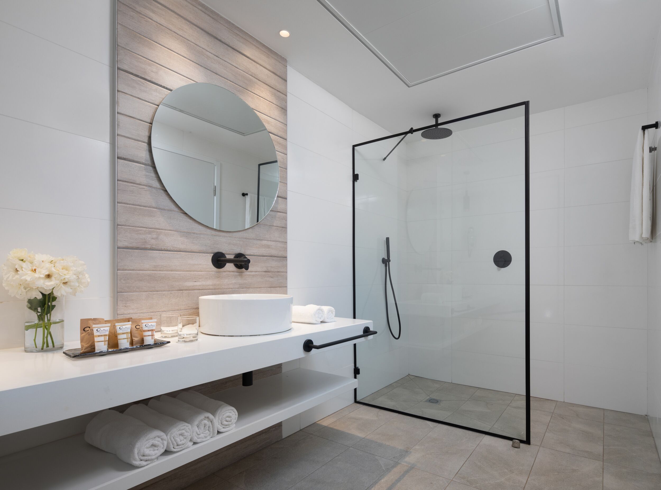 Un baño moderno con ducha envuelta en vidrio, tocador blanco con espejo y toallas ordenadas.