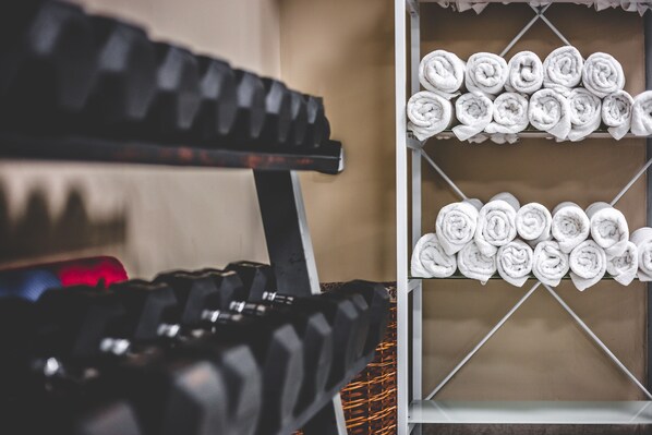 A gym with a rack of dumbbells and a shelf of neatly rolled towels.