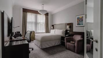Habitación de hotel con una cama grande, un escritorio con una computadora portátil, una silla, una mesita de noche y un cuadro en la pared.