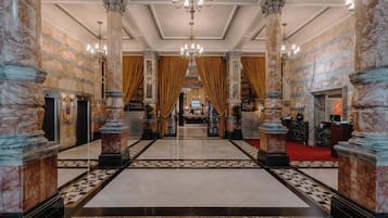 A grand lobby with marble columns, a chandelier, and a checkered floor pattern.