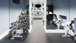 Ein Fitnessstudio mit Trainingsgeräten, darunter Kurzhanteln, Laufbänder und ein Ergometer.