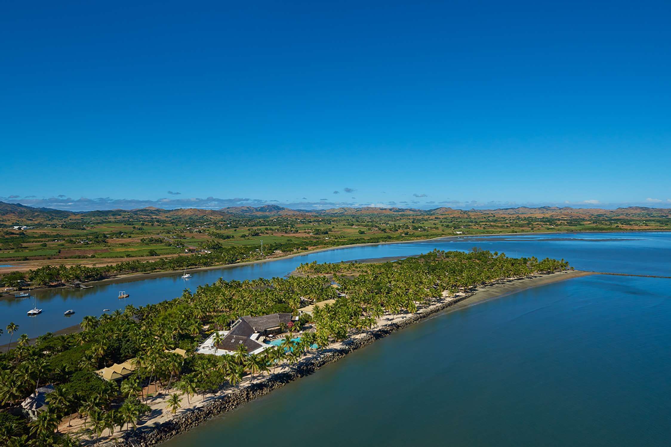 An aerial view of a coastal area with a beach, palm trees, and boats.