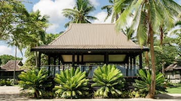 A traditional wooden structure with a sloped roof, surrounded by lush tropical vegetation.