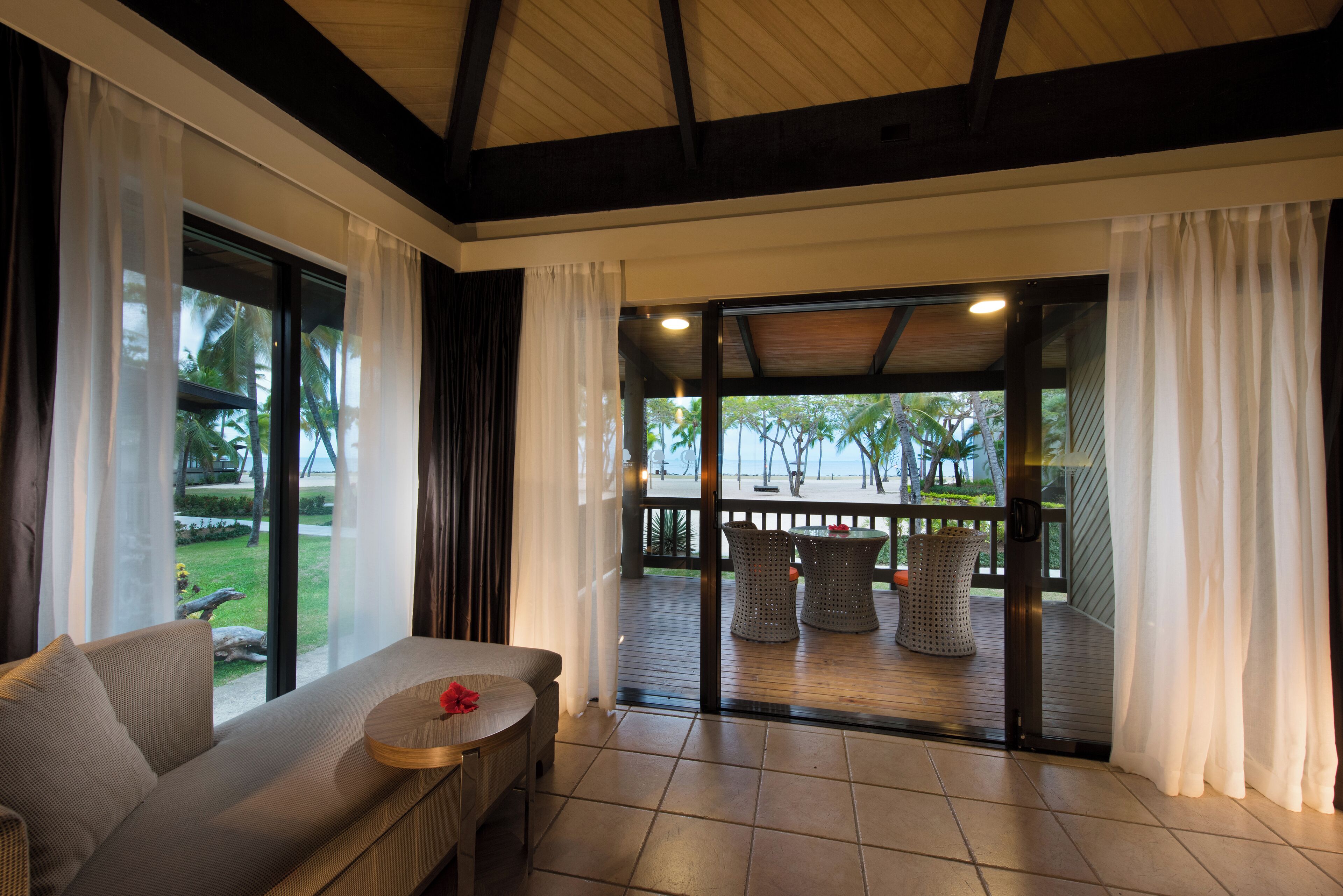 A modern room with a sofa, a small table, and a view of an outdoor deck with wicker furniture.