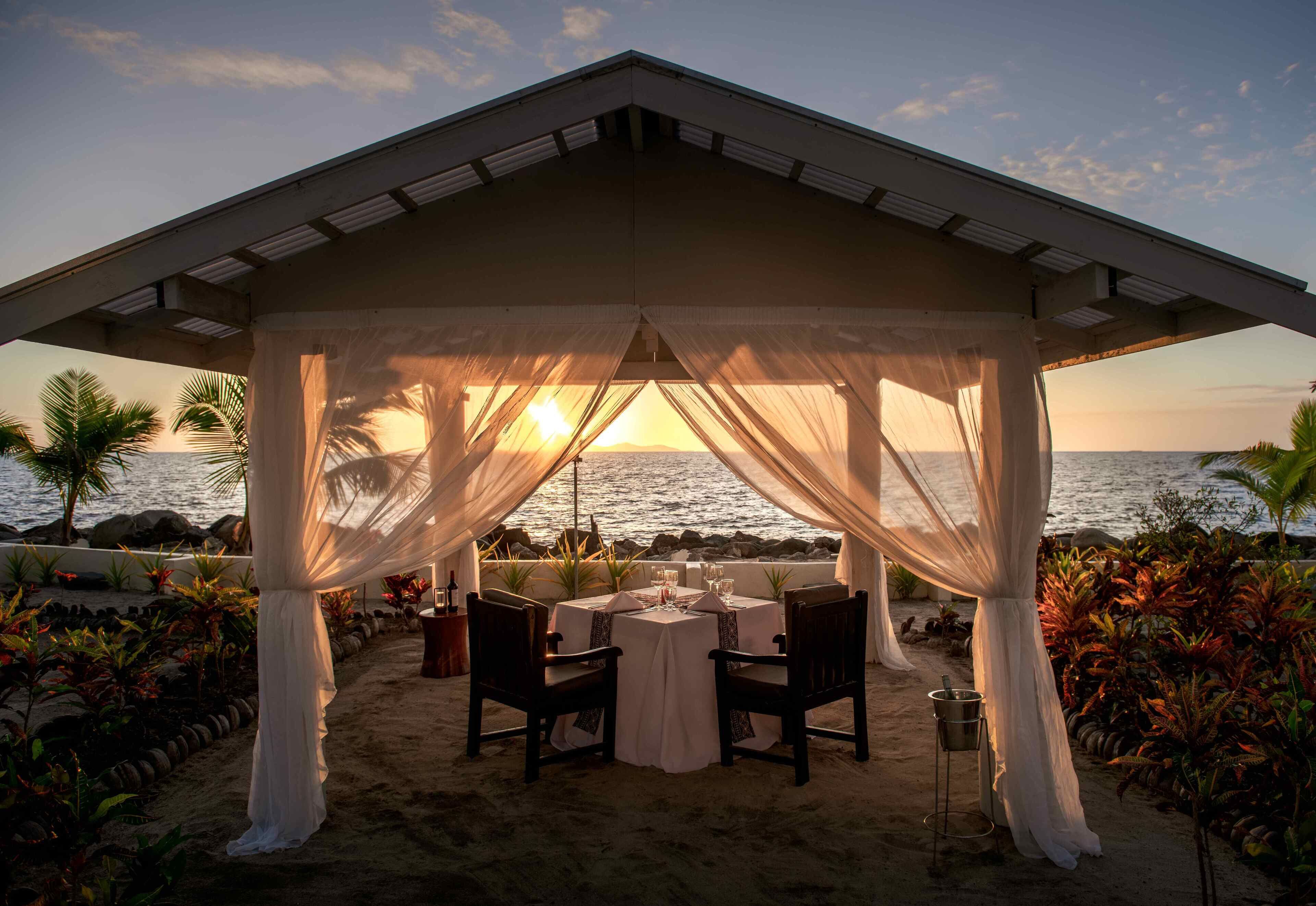 An outdoor dining area with a view of the ocean, covered by a canopy, and furnished with tables and chairs.