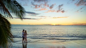 A couple standing on a beach at sunset with palm trees and the ocean in the background. - DoubleTree Resort by Hilton Hotel Fiji - Sonaisali Island (Sonaisali Island)