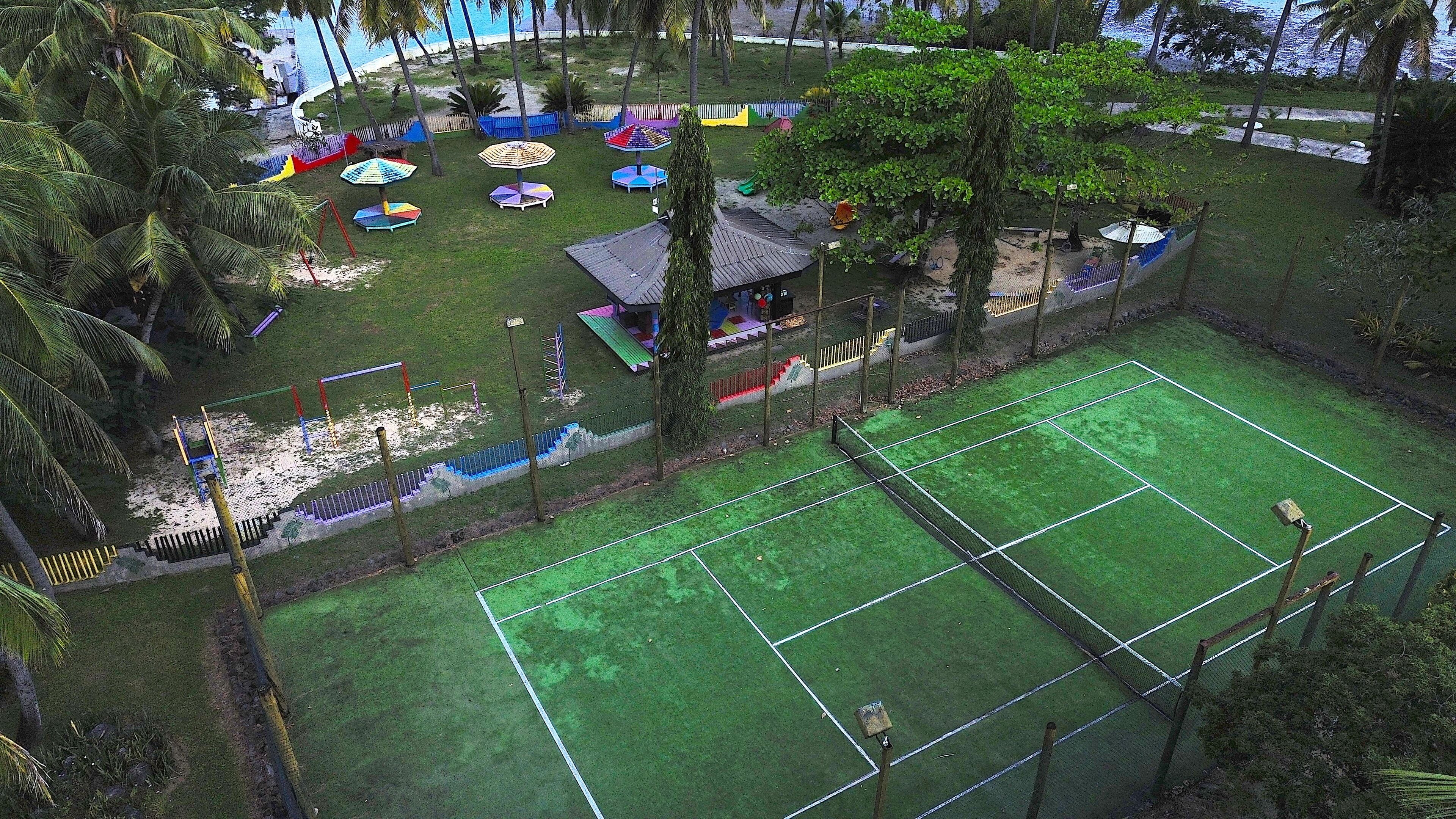 Ein Sportplatz mit umgebender Zäunung, Bäumen und einem Spielplatz mit bunten Geräten.