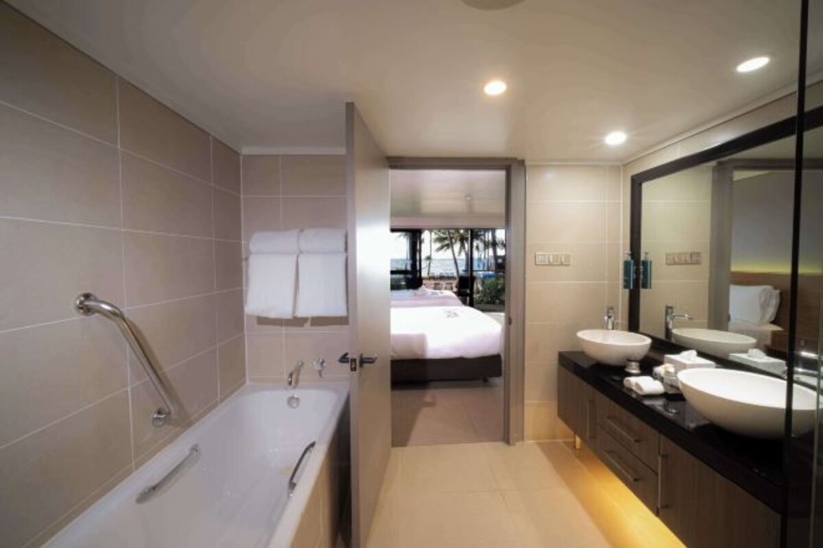 A modern bathroom with a bathtub, two sinks, and a large mirror.