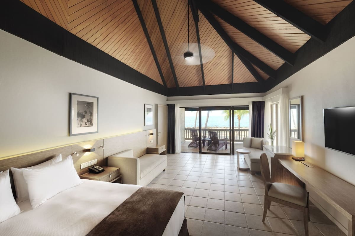 A hotel room with a bed, desk, chair, TV, and a balcony with a view.