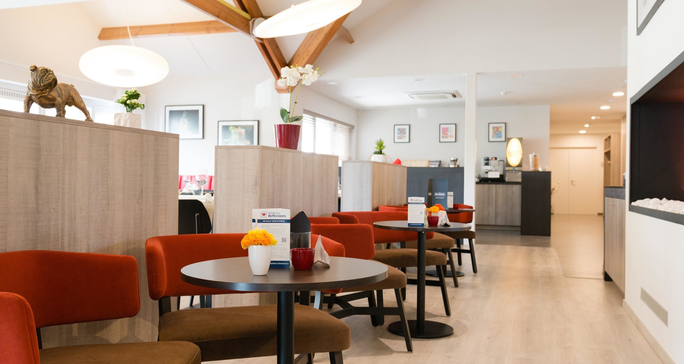 A modern restaurant with round tables and orange chairs, a wooden ceiling, and a counter area in the background.