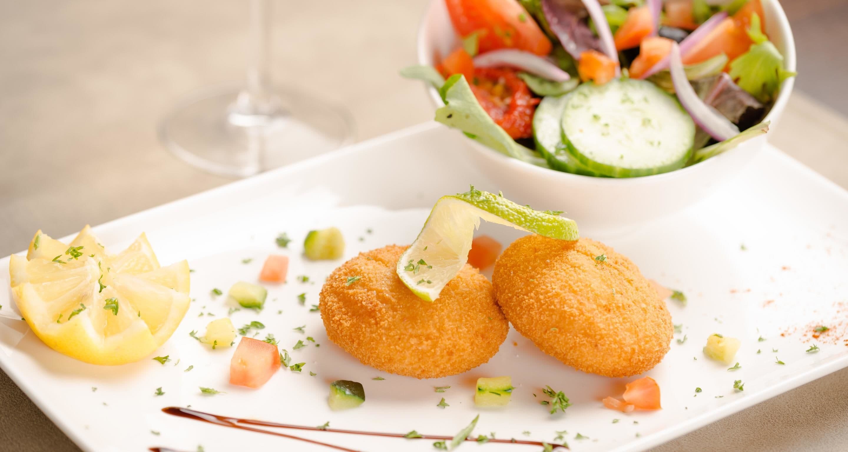 A plate with two breaded items, a lemon slice, and a salad.