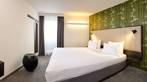 A hotel room with a large bed, a round black side table, a mirror, and a green textured wall. - Best Western Hotel Wavre (Wavre)