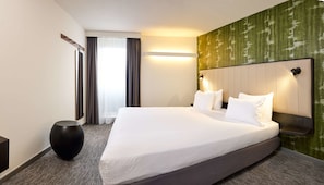 A hotel room with a large bed, a round black side table, a mirror, and a green textured wall. - Best Western Hotel Wavre (Wavre)