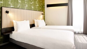 A hotel room with two beds, a green textured wall, a large window with curtains, and a nightstand with a lamp. - Best Western Hotel Wavre (Wavre)