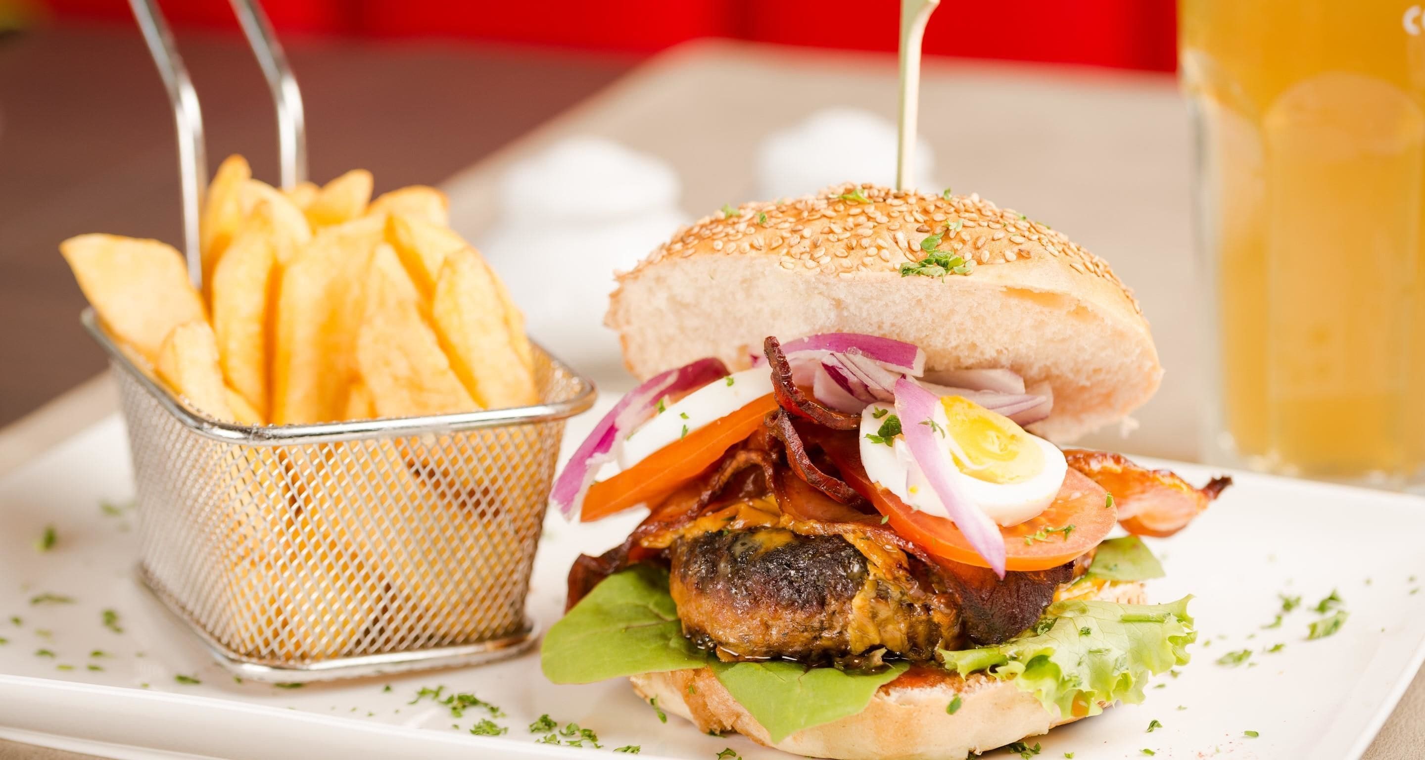 Een hamburger met bacon, tomaat en sla, geserveerd met een mand friet en een glas bier.