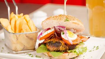Een hamburger met bacon, tomaat en sla, geserveerd met een mand friet en een glas bier.