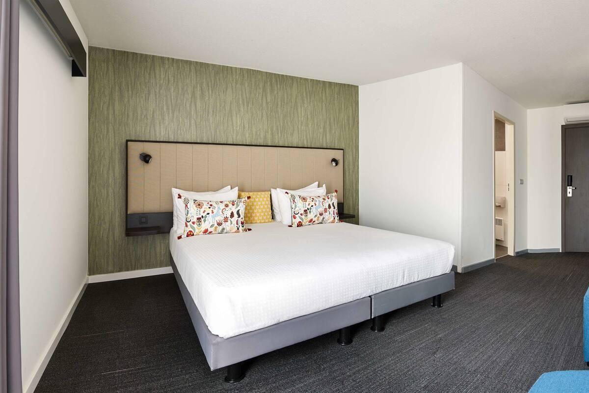 Une chambre d’hôtel avec un grand lit, une petite table et une chaise bleue.