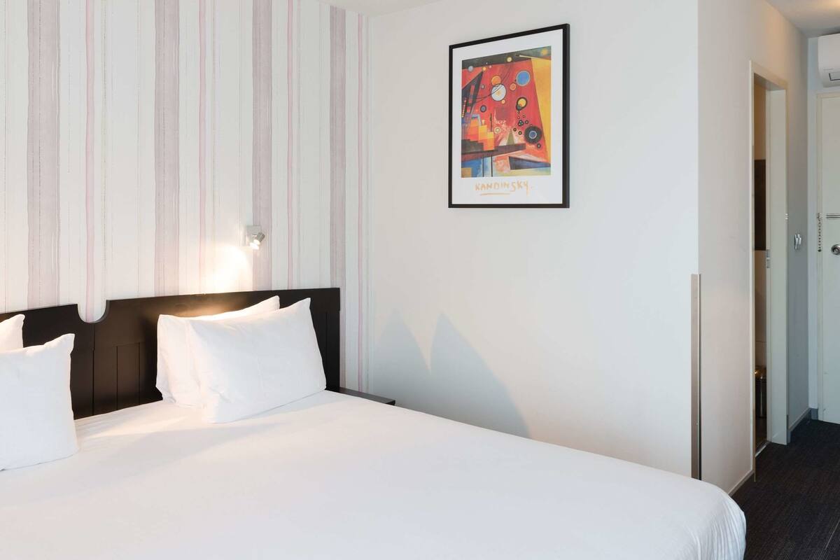 A hotel room with a bed, striped wallpaper, a framed artwork, and a door.