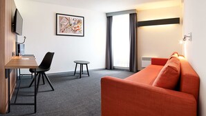 A modern hotel room with a sofa, a small table, a chair, a TV, a framed abstract painting, and a window with curtains. - Best Western Hotel Wavre (Wavre)