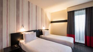 A hotel room with two beds, a nightstand, a wall-mounted light, and a window with curtains.