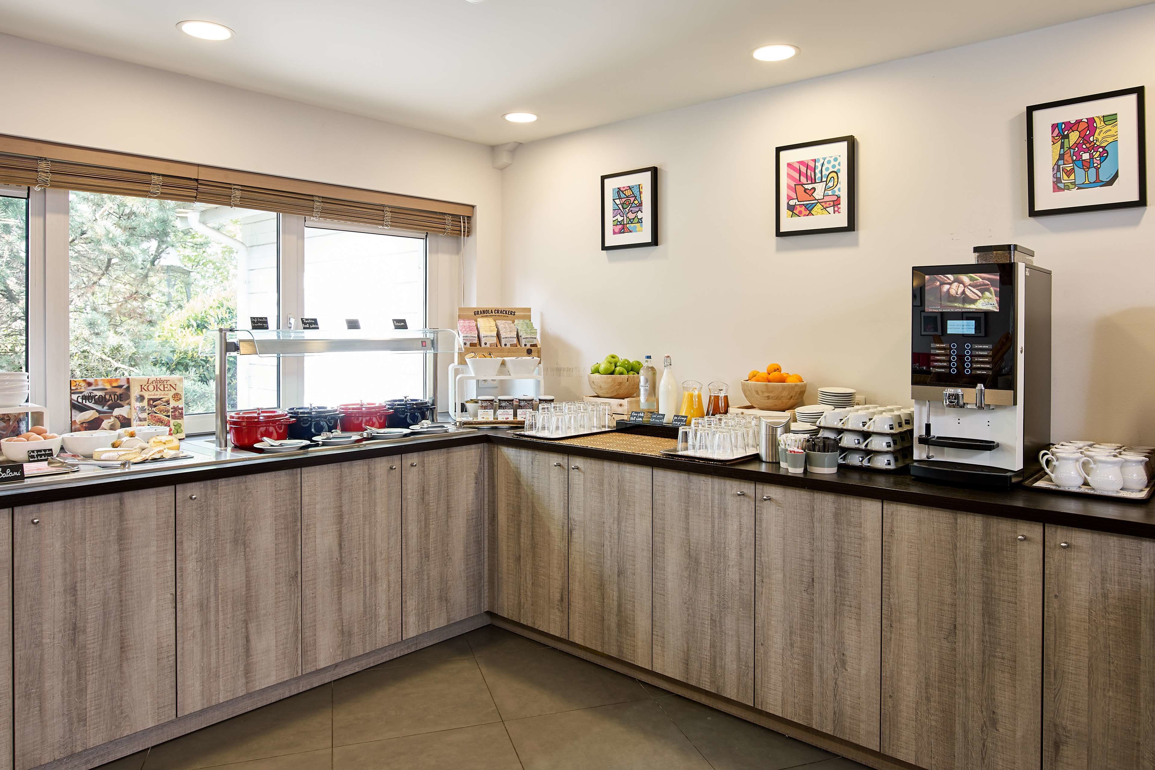 Una zona de cocina con cafetera, diversos alimentos y una ventana con persianas.