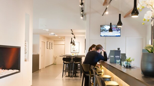 A modern kitchen with a bar area, wooden beams, and a TV on the wall. - Best Western Hotel Wavre (Wavre)