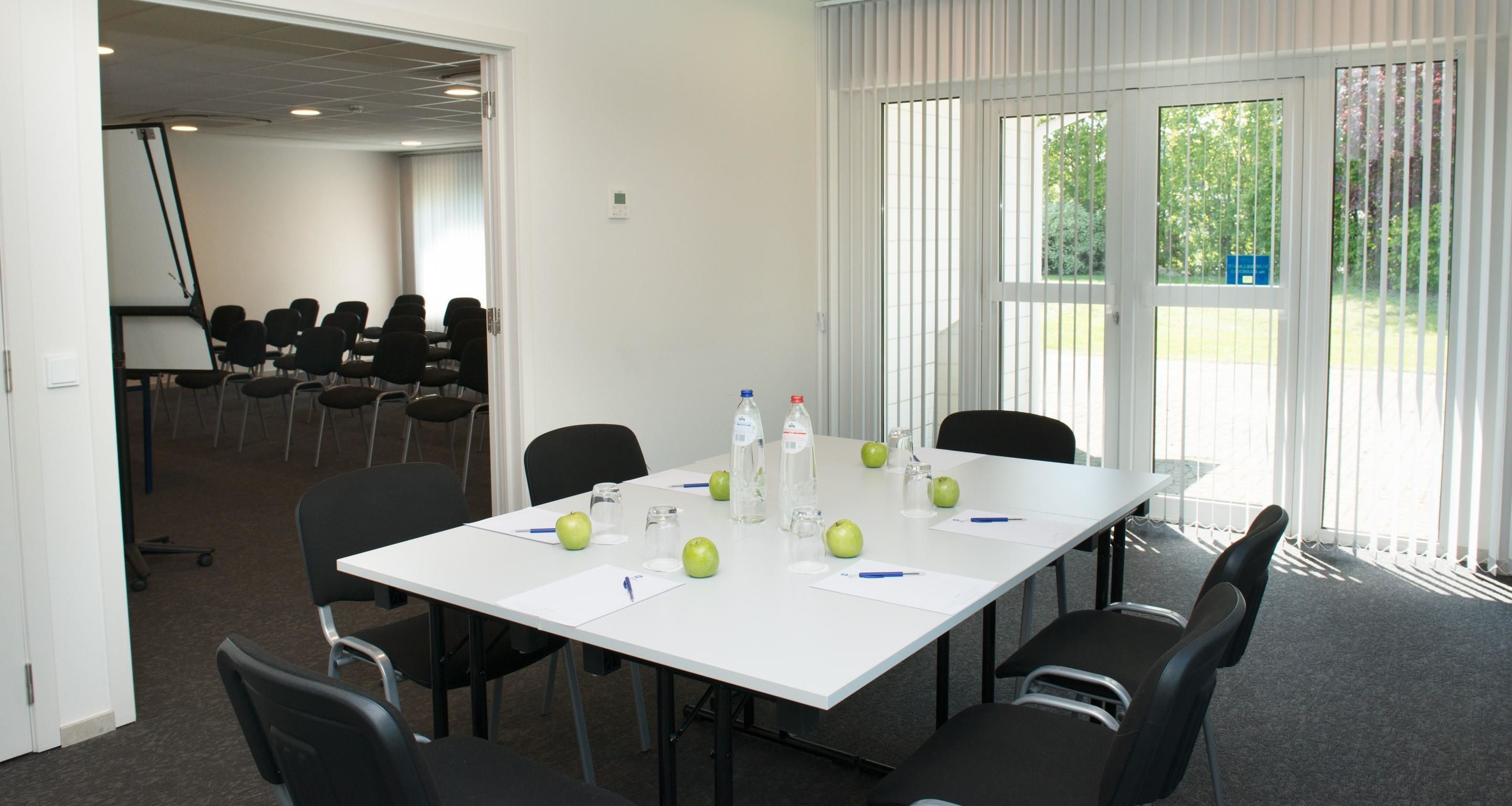 A conference room with a white table, black chairs, and a large window with blinds.