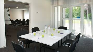 A conference room with a white table, black chairs, and a large window with blinds.