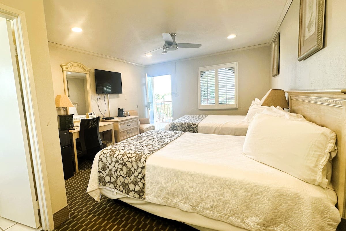A hotel room with two beds, a desk with a chair, a television, and a bathroom with a toilet.