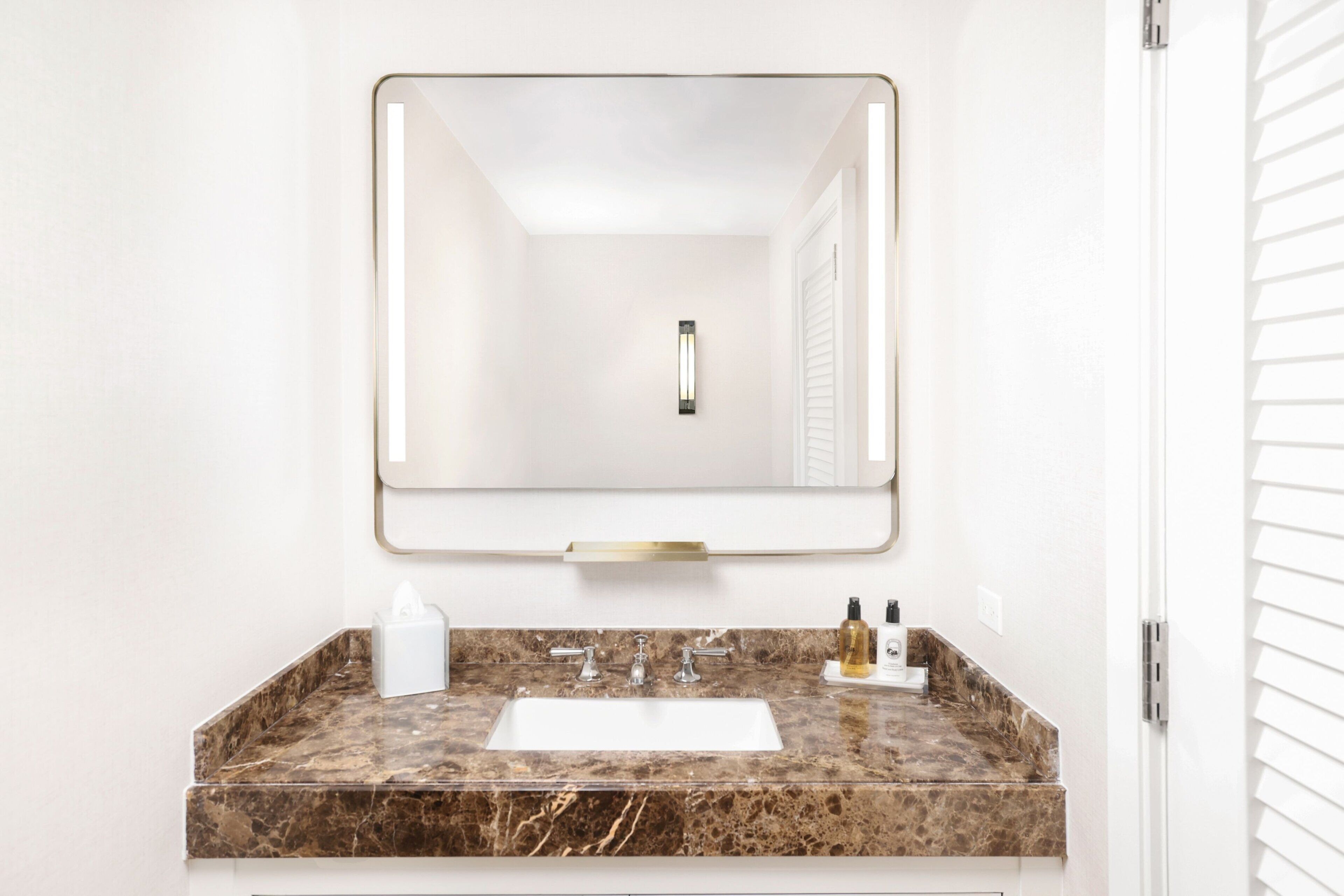 A bathroom with a marble sink, a mirror with a gold frame, and a white door with blinds.