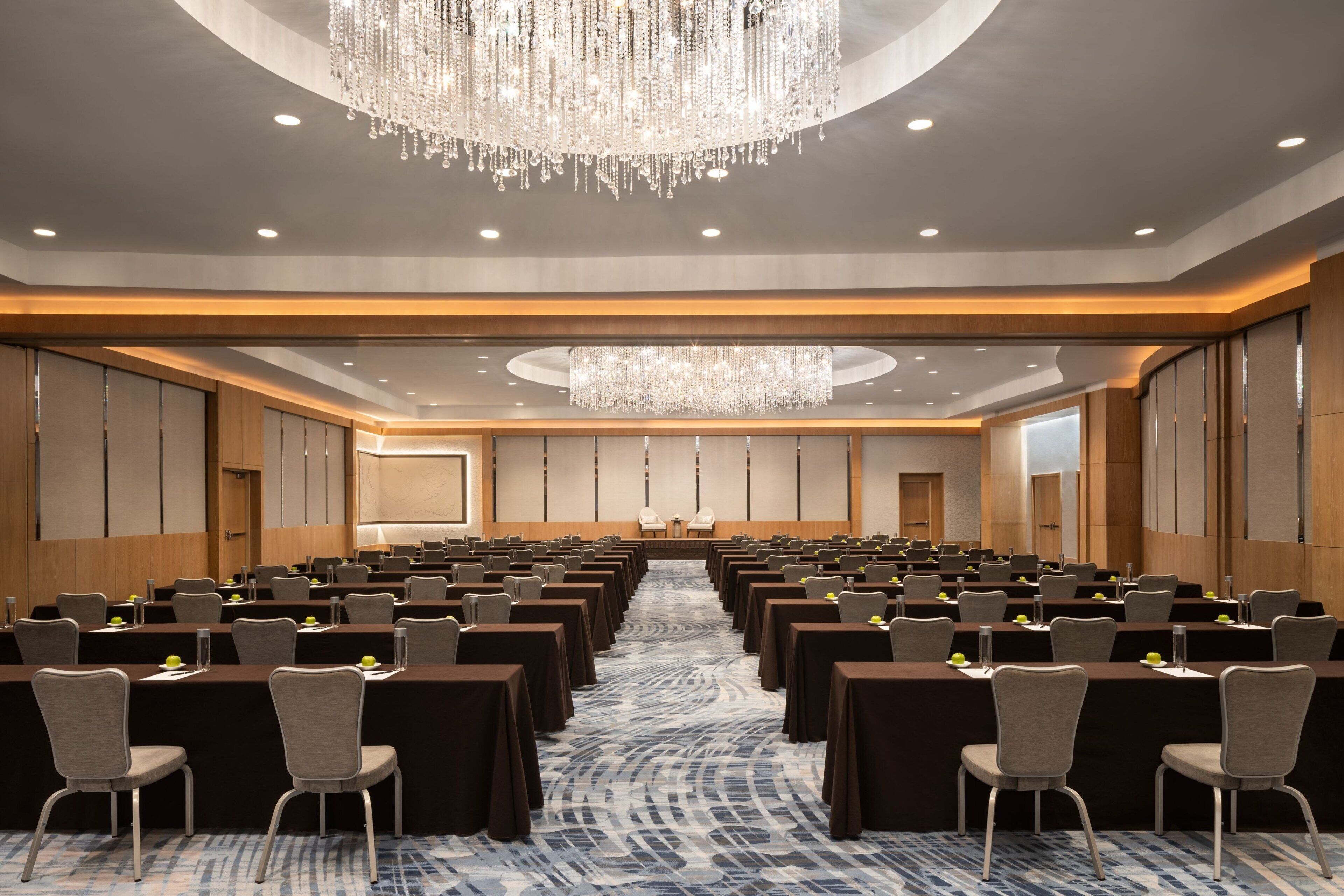A conference room with rows of tables and chairs, a large chandelier, and a patterned carpet.