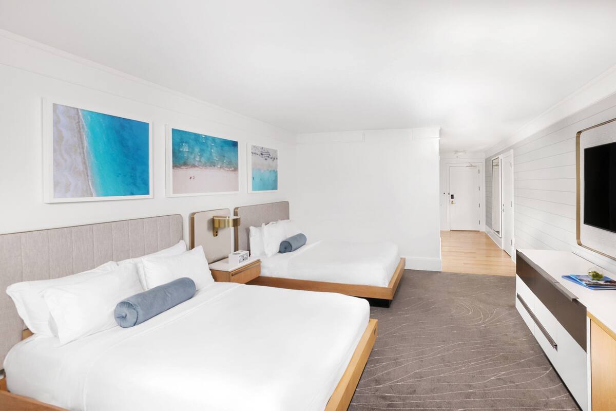 A hotel room with two beds, a TV, and artwork on the wall.
