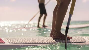 A person standing on a paddleboard in a body of water, with another person paddleboarding in the background.