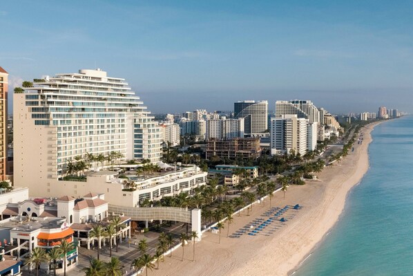 A coastal cityscape with a beachfront hotel featuring a modern design, a promenade lined with palm trees, and a clear view of the ocean. - The Ritz-Carlton, Fort Lauderdale (Fort Lauderdale)