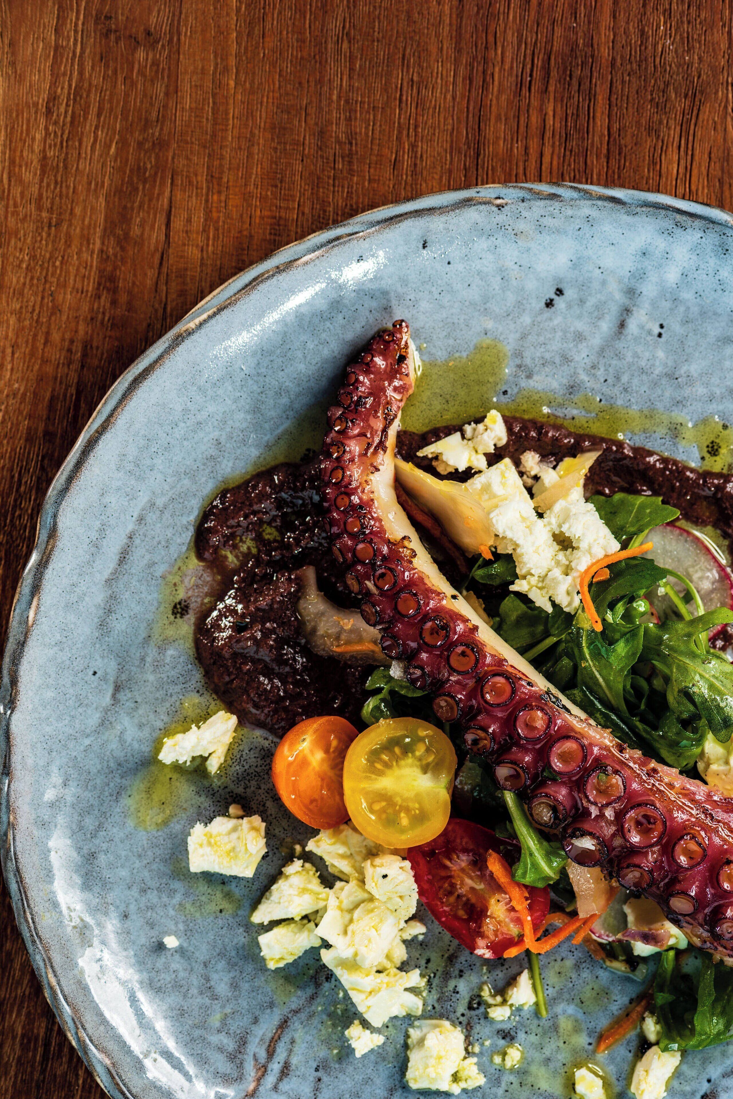 A plate with octopus, cherry tomatoes, and greens.