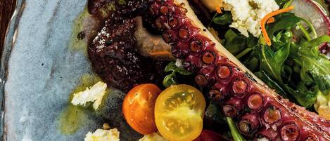 A plate with octopus, cherry tomatoes, and greens.
