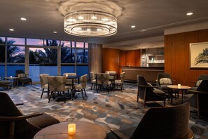 A hotel lobby with a chandelier, seating area, and large windows with a view of palm trees. - The Ritz-Carlton, Fort Lauderdale (Fort Lauderdale)