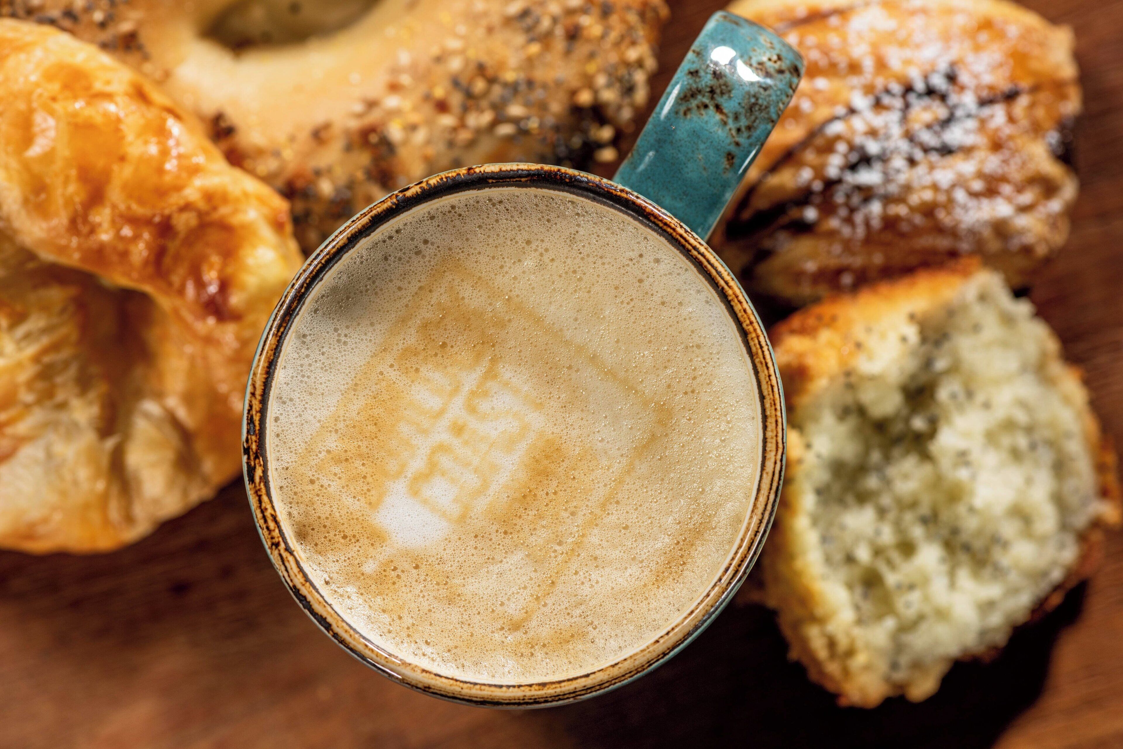 A cup of coffee with a frothy top, surrounded by various pastries.