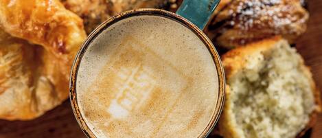 A cup of coffee with a frothy top, surrounded by various pastries.