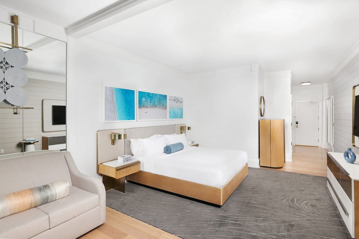 A modern hotel room with a large bed, a sofa, a desk, and a TV.
