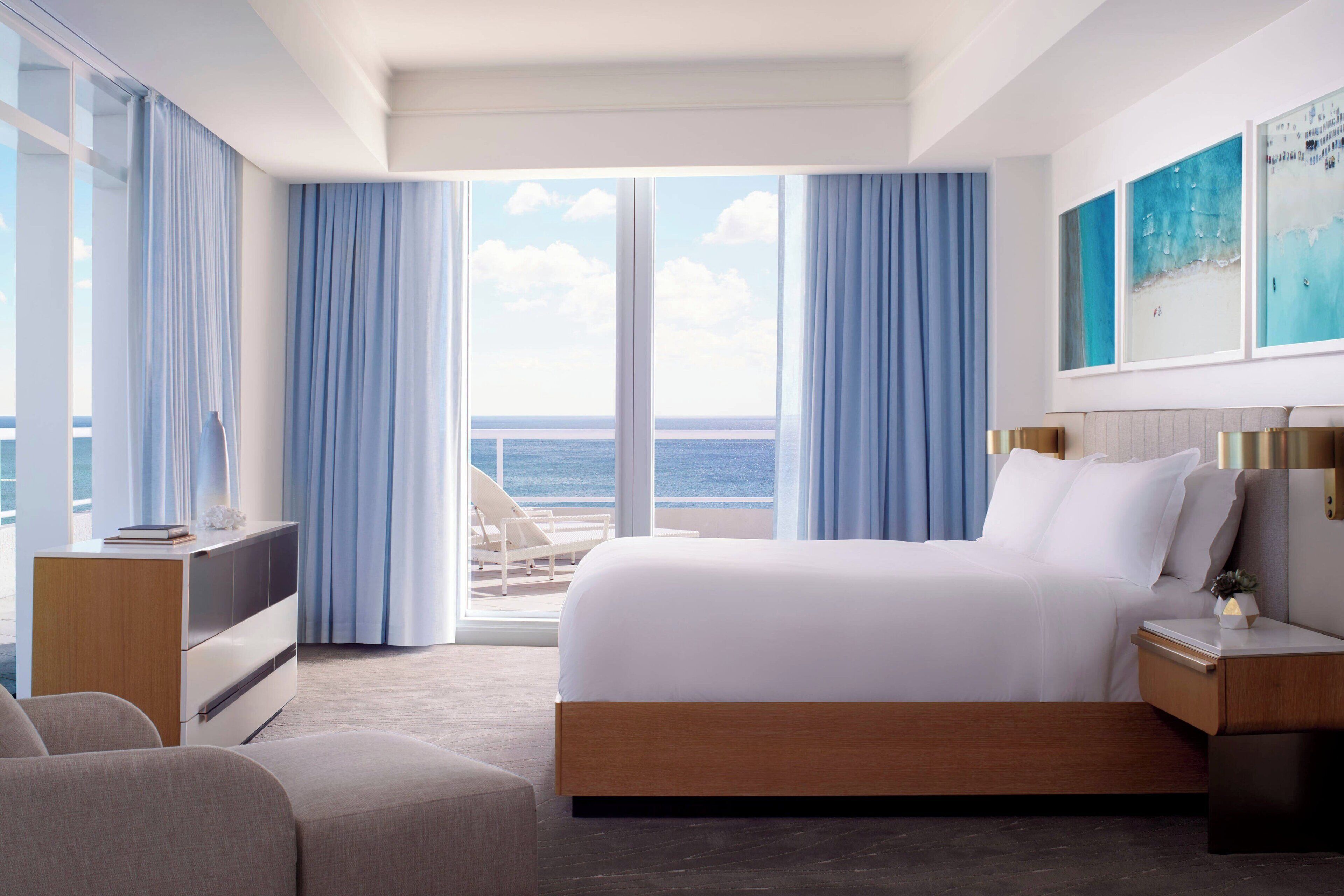 A modern hotel room with a large bed, a desk, and a view of the ocean.