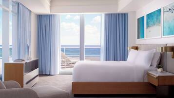 A modern hotel room with a large bed, a desk, and a view of the ocean.