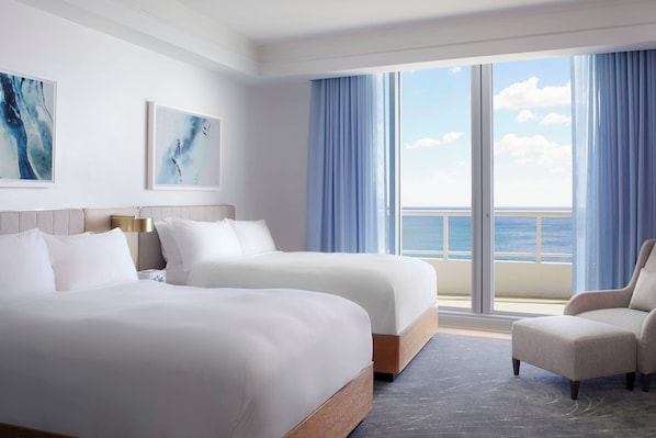 Habitación de hotel con dos camas, una silla y un ventanal con vistas al mar.