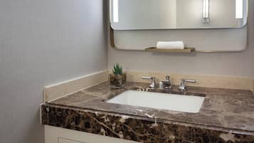 A bathroom with a marble sink, a mirror, and a small potted plant.