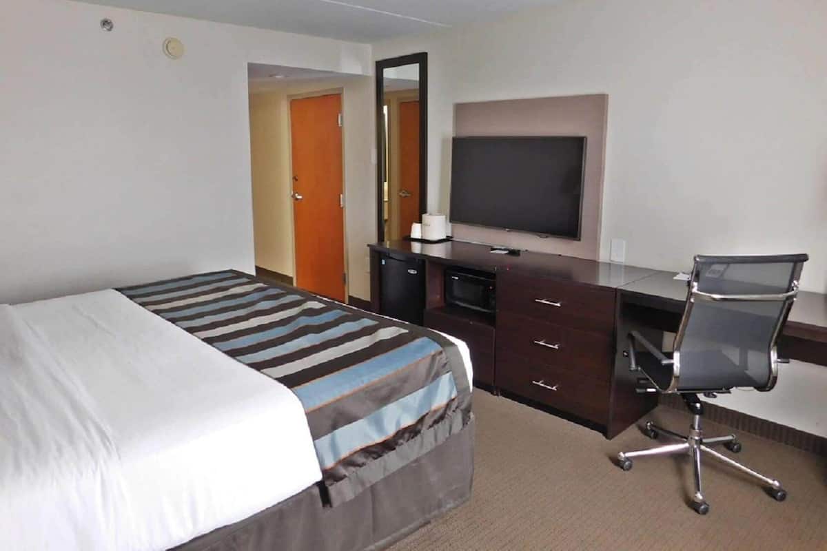 Ein Hotelzimmer mit Bett, Schreibtisch, Stuhl, Fernseher und Spiegel.