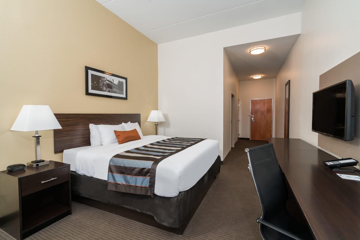 Ein Hotelzimmer mit Bett, Nachttischlampen, Fernseher, Schreibtisch und einem gerahmten Bild an der Wand.