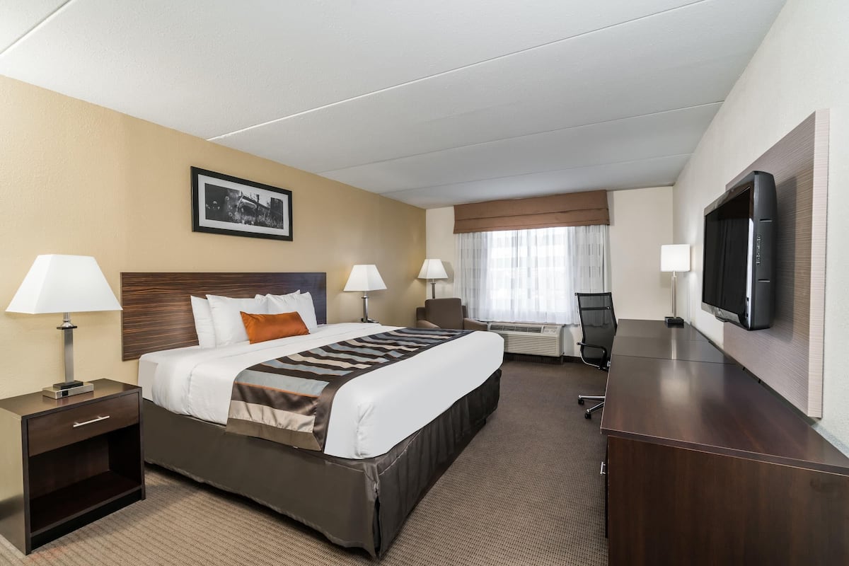 Ein Hotelzimmer mit Bett, Nachttischen, Lampen, Schreibtisch, Stuhl, Fernseher und einem Fenster mit Vorhängen.