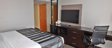 Une chambre d’hôtel équipée d’un lit, d’un bureau avec un ordinateur, d’une chaise, d’une télévision et d’un mini-bar.