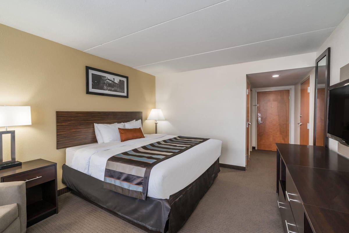 Ein Hotelzimmer mit einem Bett, Nachttischen, einem Fernseher und einer Tür zu einem anderen Raum.